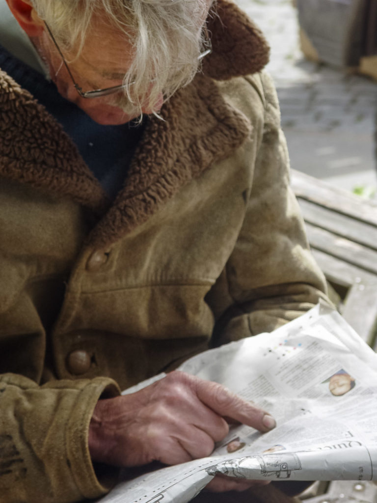 Before smart phones, a lot of people read newspapers. This is an older man reading a newspaper on the street.