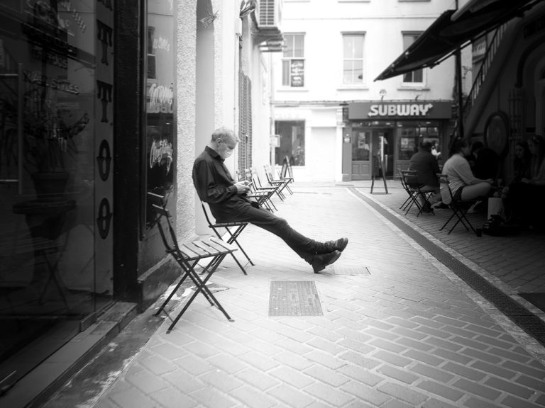 At the height of the Covid19 Pandemic in July 2020, someone takes a break out in the open of a narrow street wearing a mask while he looks at his phone.