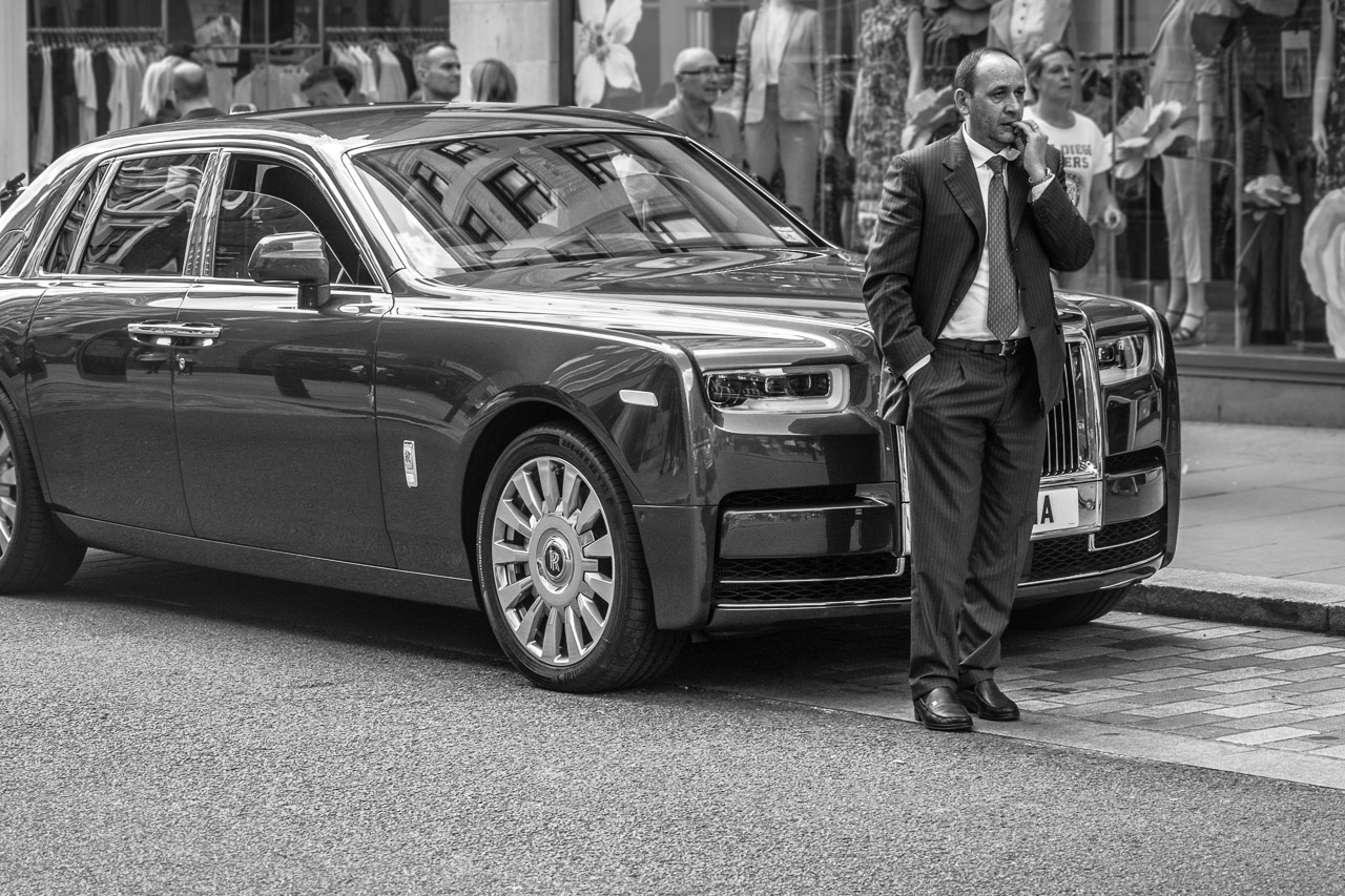 A chauffeur stands nervously in front of his Rolls Royce car in London, waiting and biting his nails.