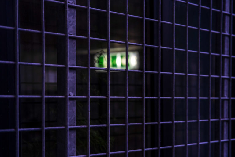An emergency exit inside a darkened room, with a wire fence over the window.