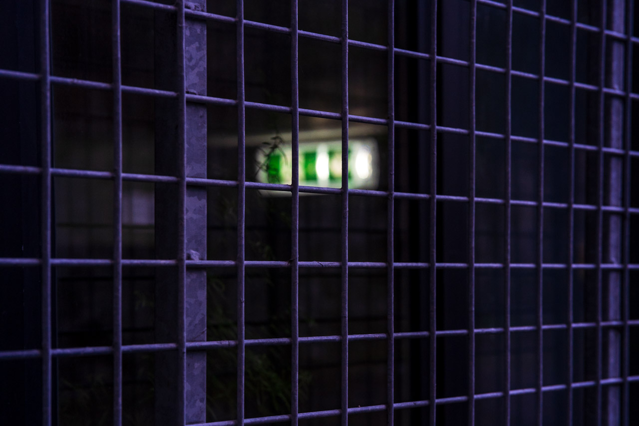 An emergency exit inside a darkened room, with a wire fence over the window.
