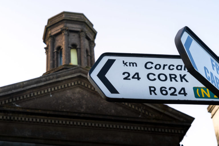 A sign points to Cork, 24KM away. The old Methodist church in Cobh in the background.