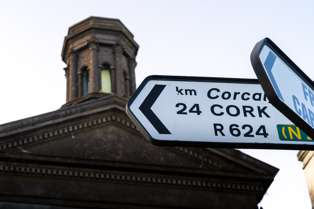 A sign points to Cork, 24KM away. The old Methodist church in Cobh in the background.