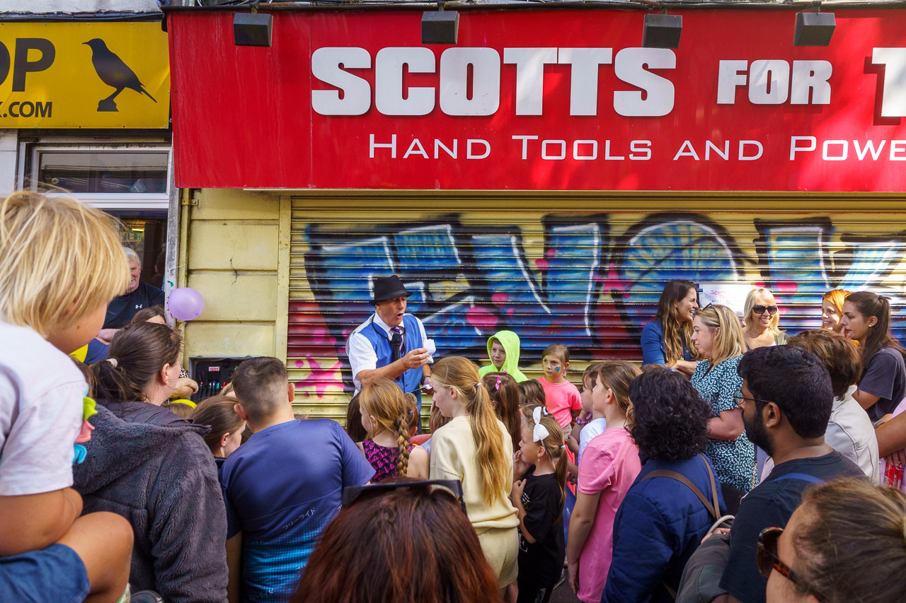 A street performer at the recent North Main Street festival in late August has the attention of young and old. He's standing in front of "Scotts For Tools", a DIY shop.