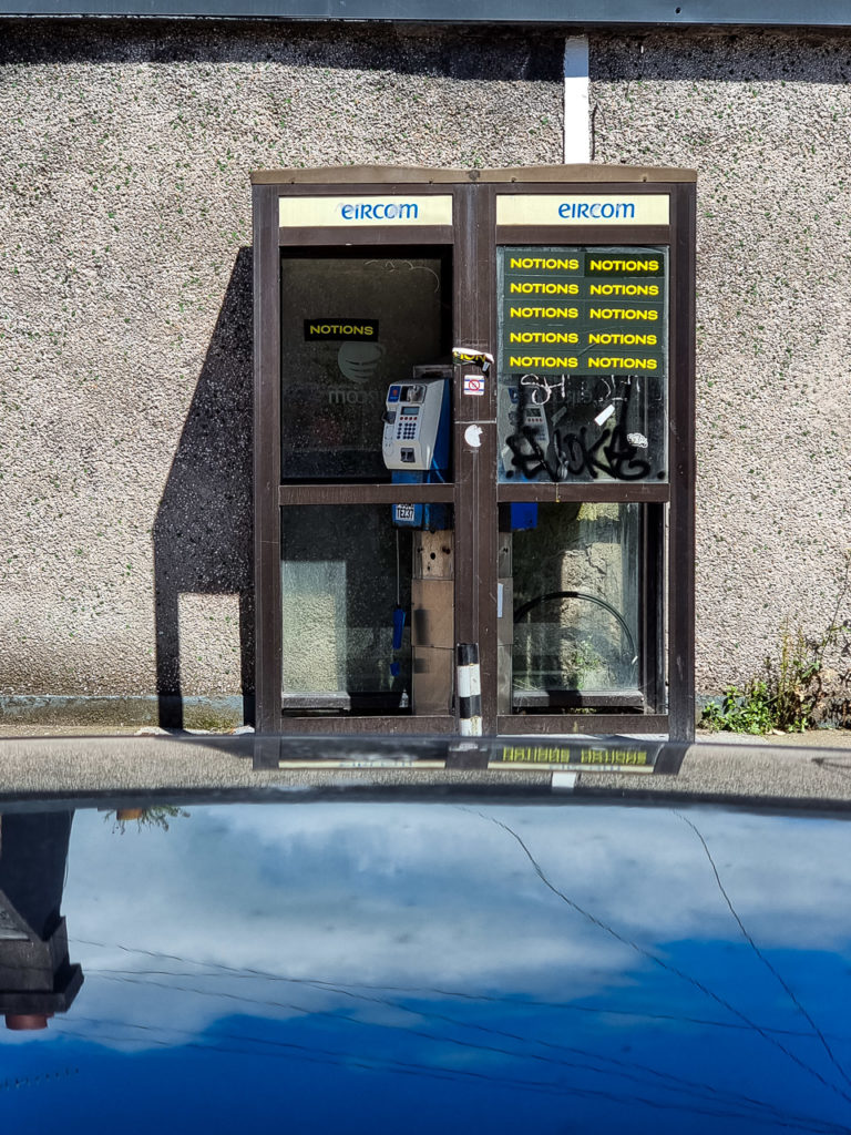 A double phonebox looking pretty beat up. The phones belong to Eircom, but "NOTIONS" stickers are stuck on it.