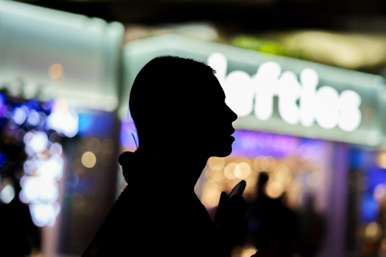 A woman silhouetted by the lights of nearby shops.