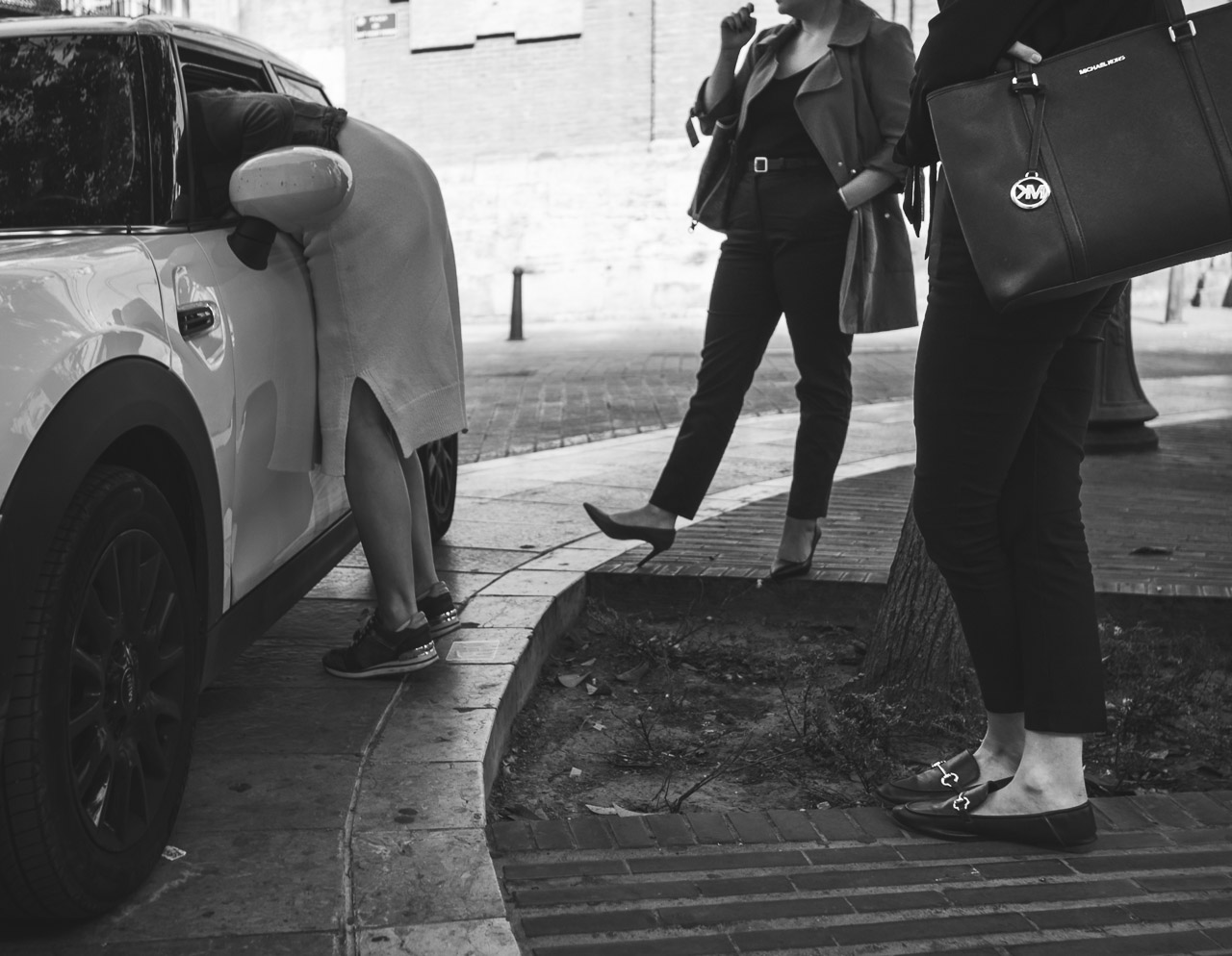 A woman looks in her car while her two friends wait for her.
