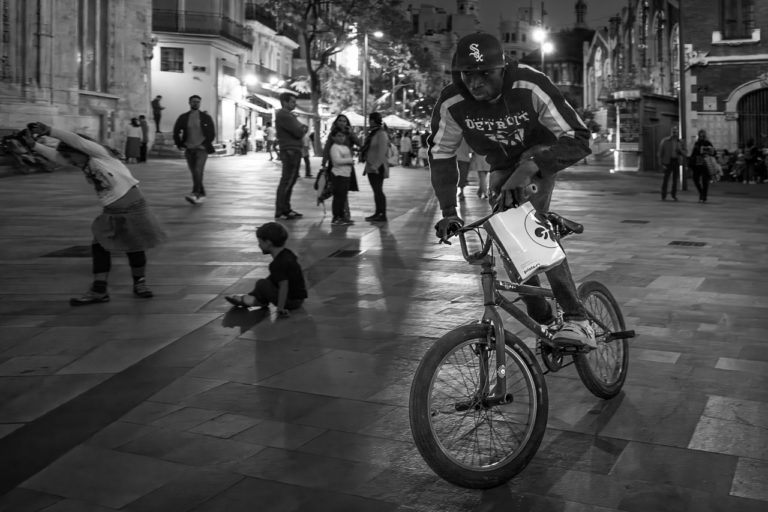 A cyclist is frozen in motion as he speeds past me. Lots of people in the background.