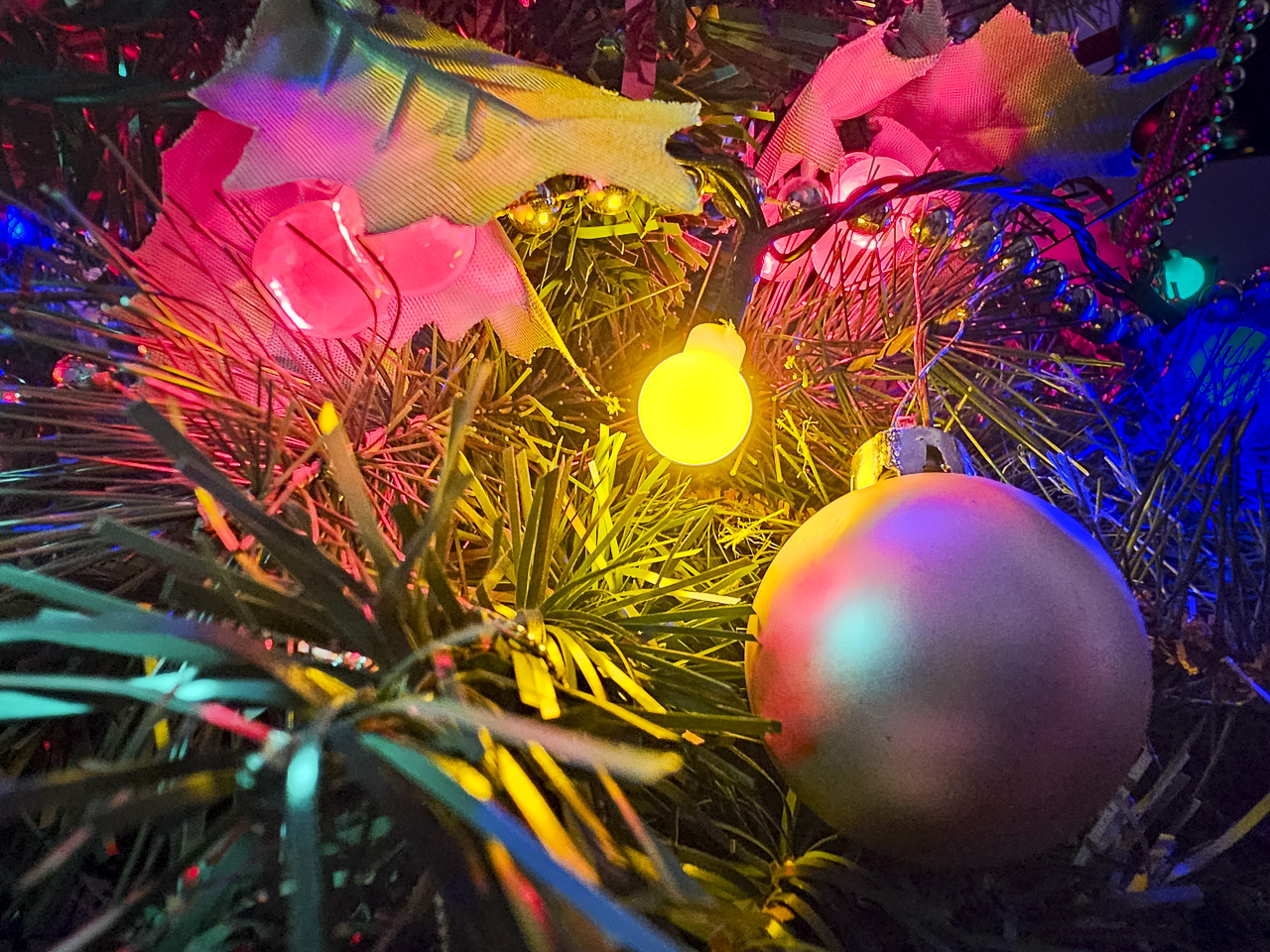 A glowing yellow light brightens a Christmas tree, surrounded by decorations.