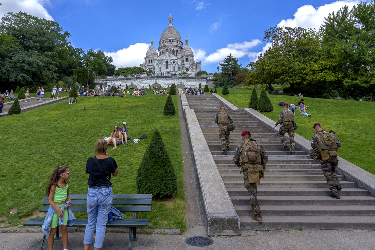 Four soldiers walk up the steps of Montmarte. People are relaxing nearby and the Basilica can be seen at the top of the hill.