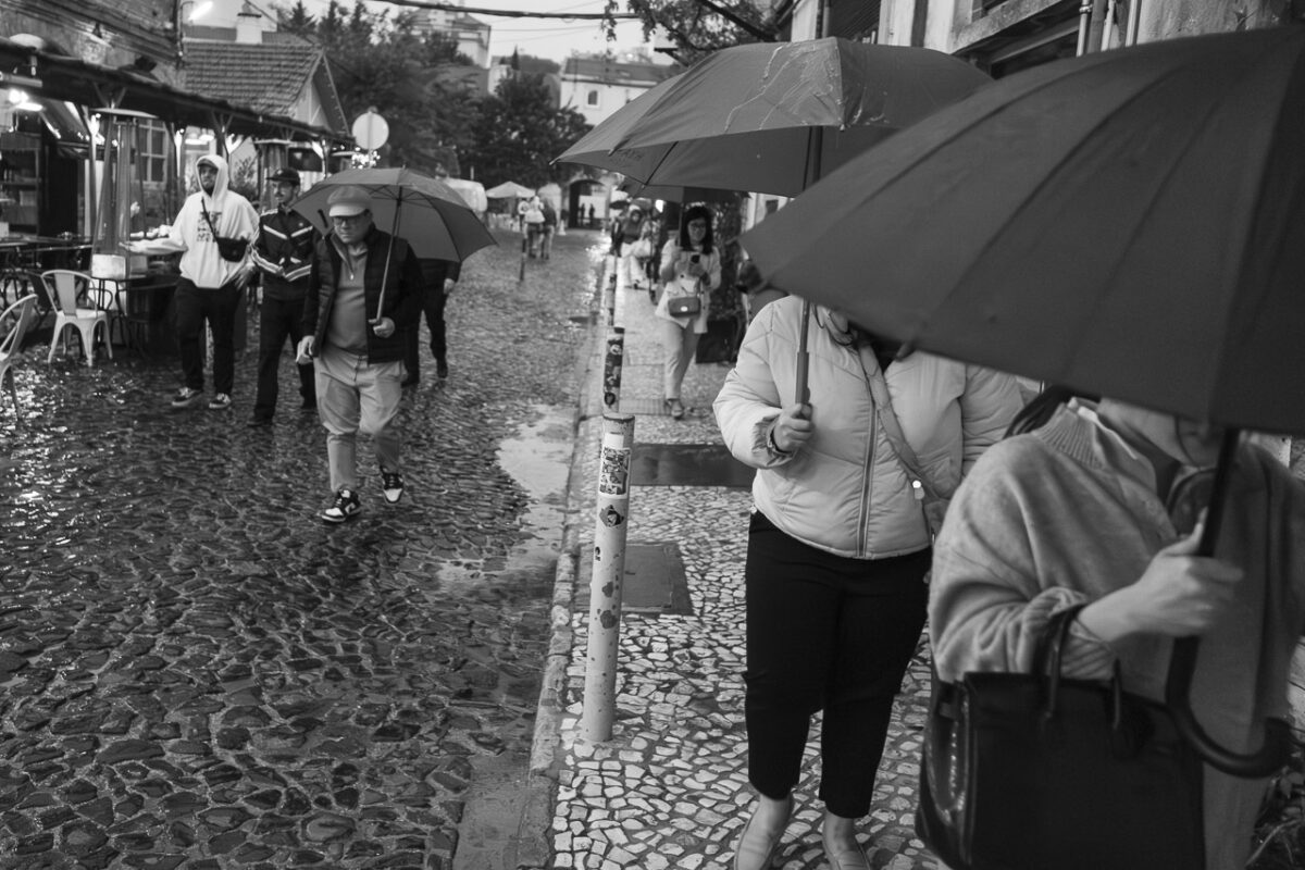 It's raining and some people are carrying umbrellas to protect themselves from the downpour. Others walk around without, along a street.