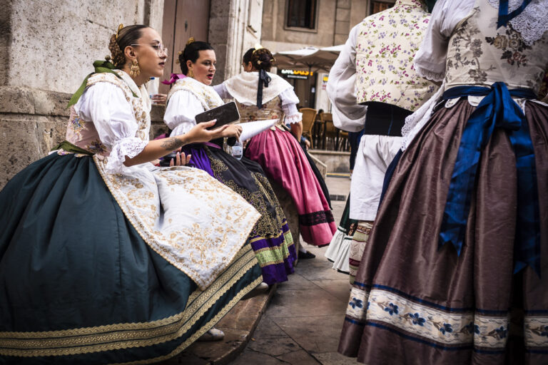 Women dressed in large, billowing, brightly lit dresses with the one in the foreground holding her phone.