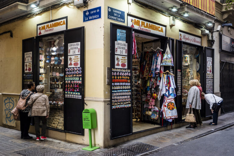 Five women look in a shop call MI FLAMENCA through two separate windows at the tourist knick knacks for sale. They're maybe unaware of each other as they are separated by a corner. A postbox sits at the corner, waiting for postcards home.