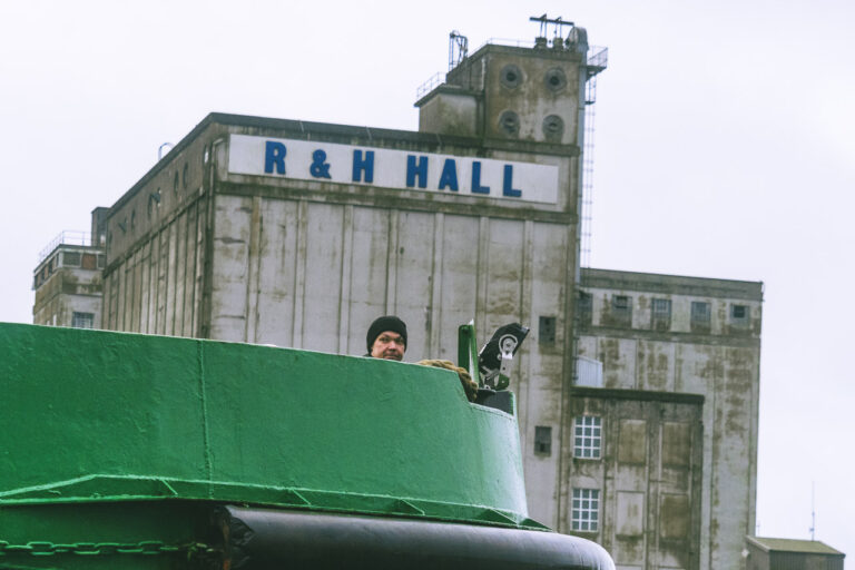 A man looks out from a boat with the massive R&H Hall building in the background.