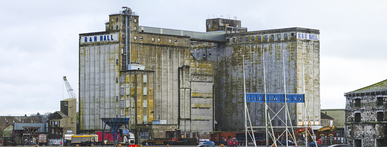The large R&H Hall building on Kennedy Quay in Cork. The back of the Welcome to Cork" sign is visible in the foreground. Other buildings and vehicles can be seen too, tiny in comparison.