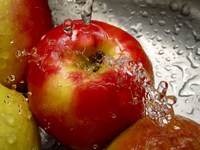 Water bounces off red apples in a sink. The stopper isn't visible, but it will stop any leaks.