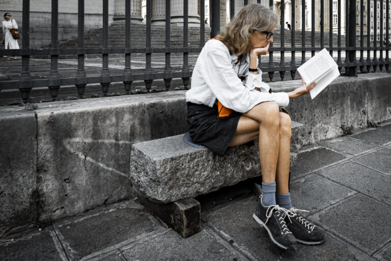 Someone sits on a rock bench, lost in a book, while in the background a woman in white seems lost in the courtyard of the Panthéon, Paris.