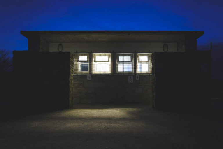 Public toilets at a beach are lit up at night in the dark. Light streams out the windows.