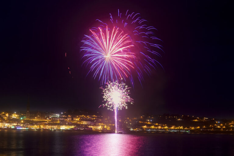 Fireworks light up the night sky over Cobh. The light reflects on the water.