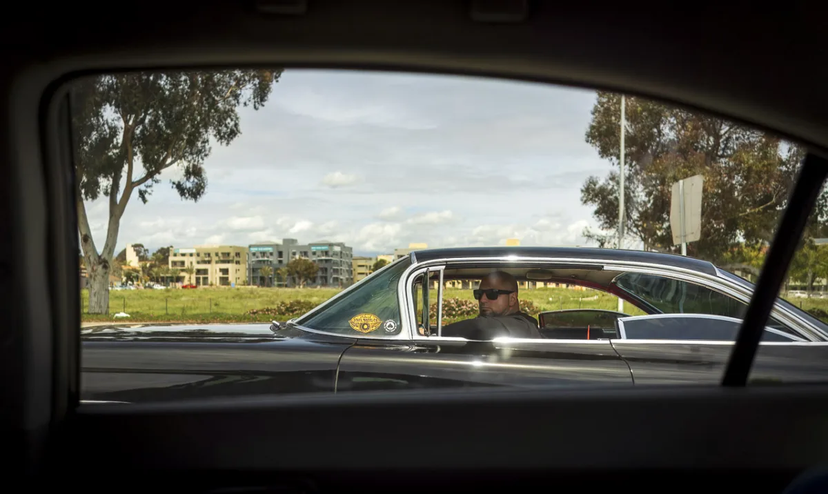 A man in sunglasses looks out from his car window as he passes us. The photo is framed by the window of the car I'm in.