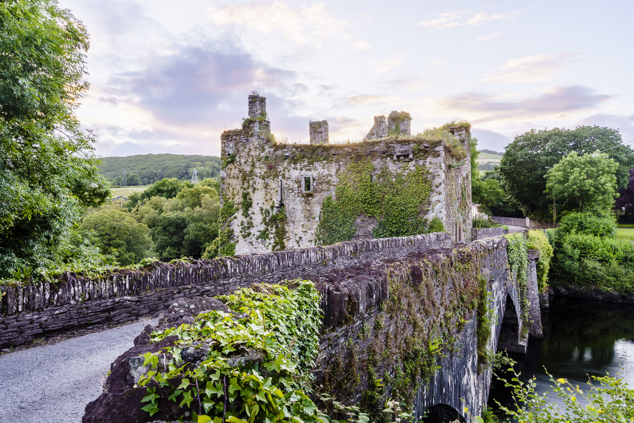 A bridge with a castle in the middle of the river. The sun has set behind it, lighting up some of the sky.