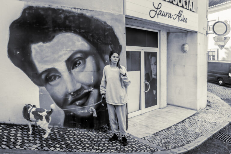 A woman brings her dog for a walk in front of a building with a large face painted on it.