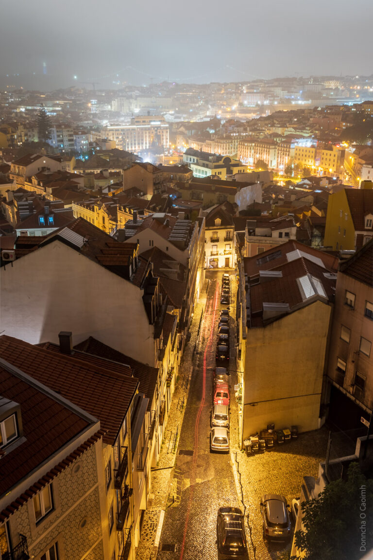A long exposure shot of Lisbon, with the trailing red brake lights of a car captured going down a nearby street.