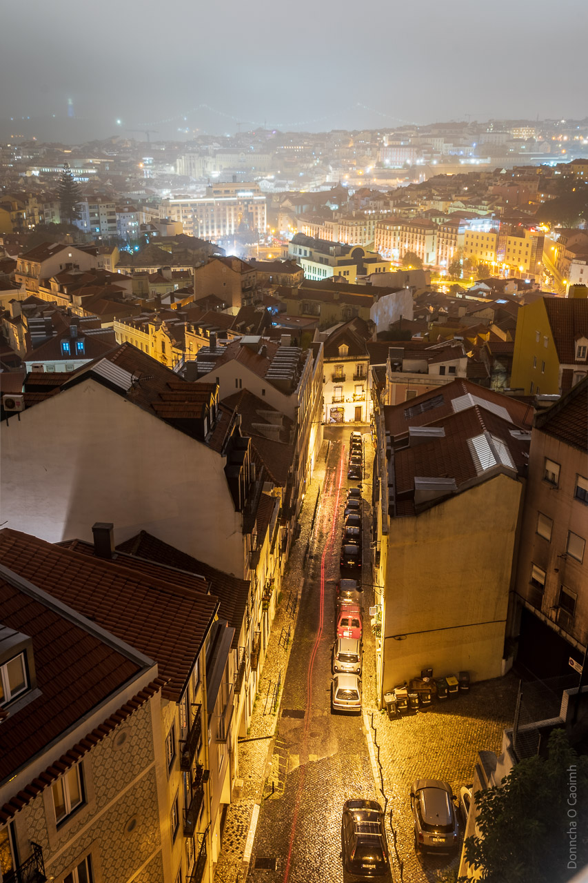 A long exposure shot of Lisbon, with the trailing red brake lights of a car captured going down a nearby street.