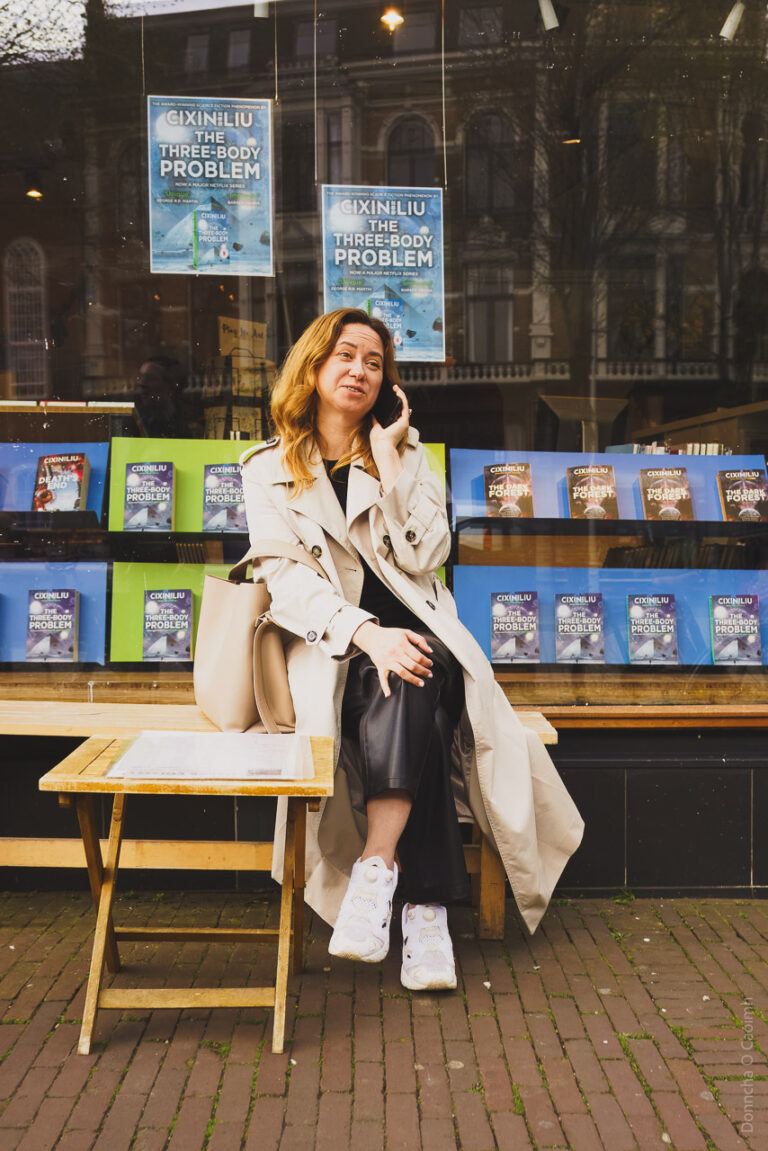 A woman on her phone, sitting outside a bookshop in Amsterdam on a cool March afternoon.