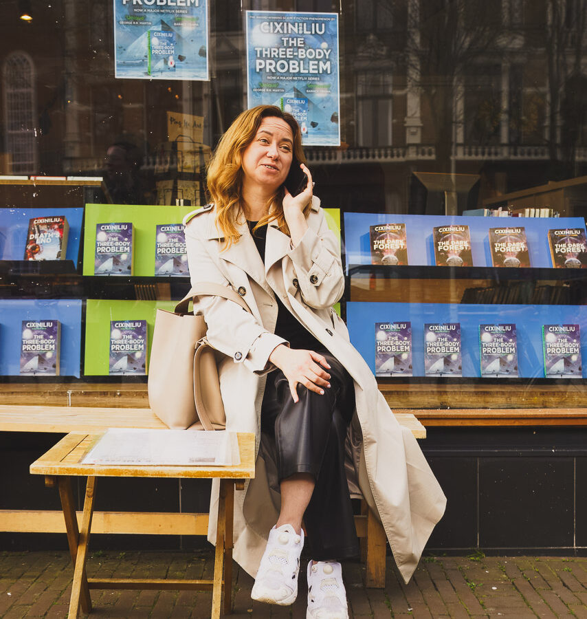 A woman on her phone, sitting outside a bookshop in Amsterdam on a cool March afternoon.