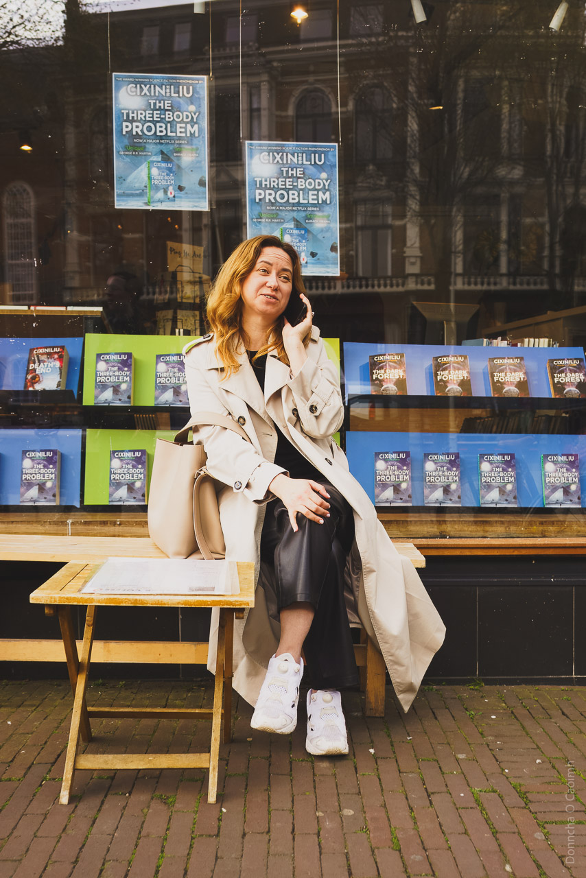 A woman on her phone, sitting outside a bookshop in Amsterdam on a cool March afternoon.