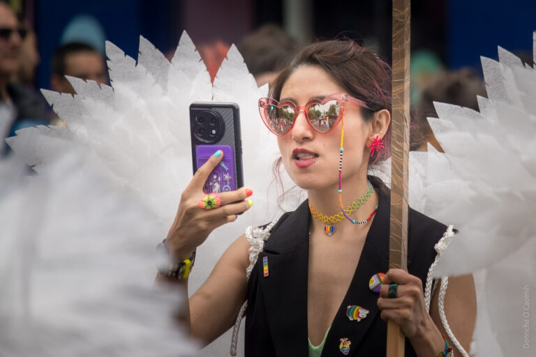 A woman with wings on her back like an angel checks her phone in the Pride parade in Cork.