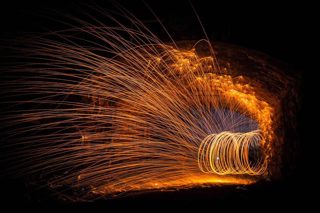 Sparks fly through the air under a bridge in a long exposure photo.