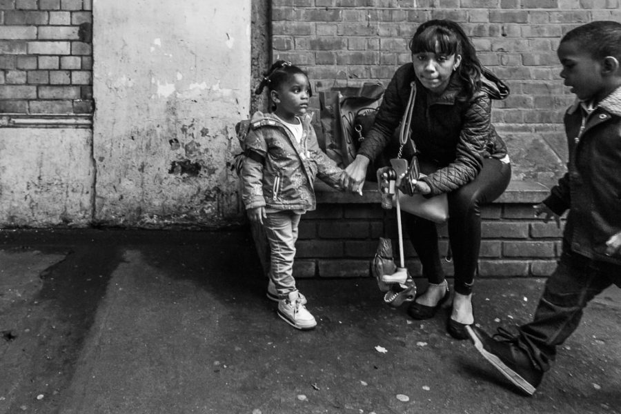 A woman holds the hand of her daughter while her son walks into the frame.