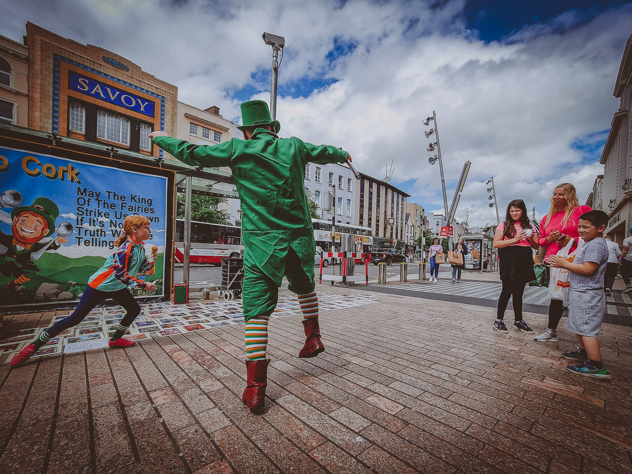 A leprechaun dancing on the street being watched by a family