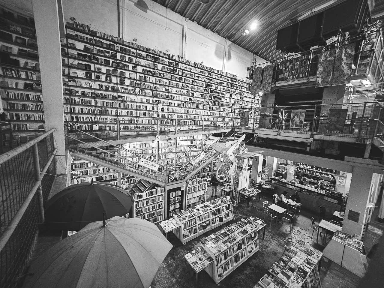 A bookshop. Shelves of books line the wall, upstairs and downstairs. Umbrellas are seen too, above the cash registers.