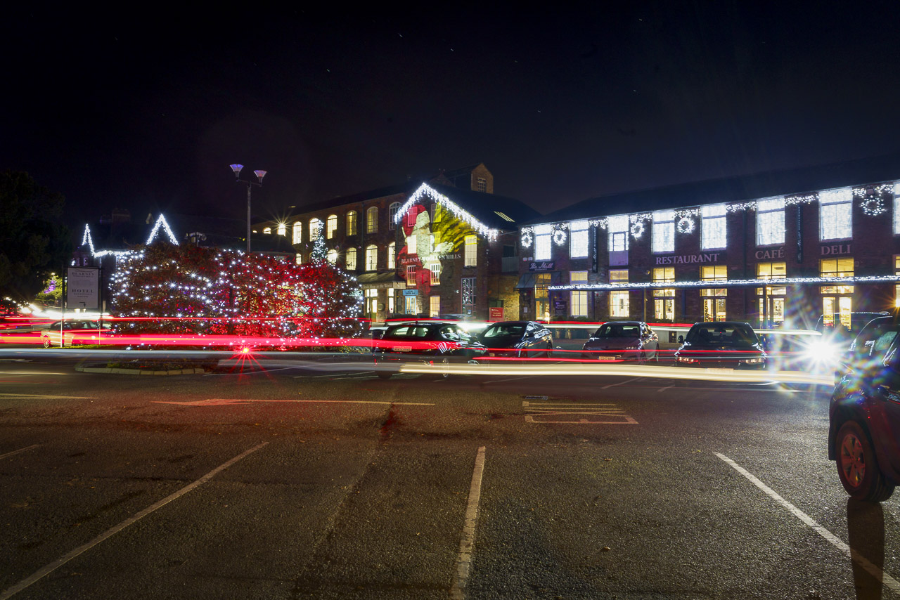 The Woollen Mills and Christy's Bar in Blarney are decorated in lights for the season. Cars are parked out front and light trails from passing cars are captured in a long exposure photo.