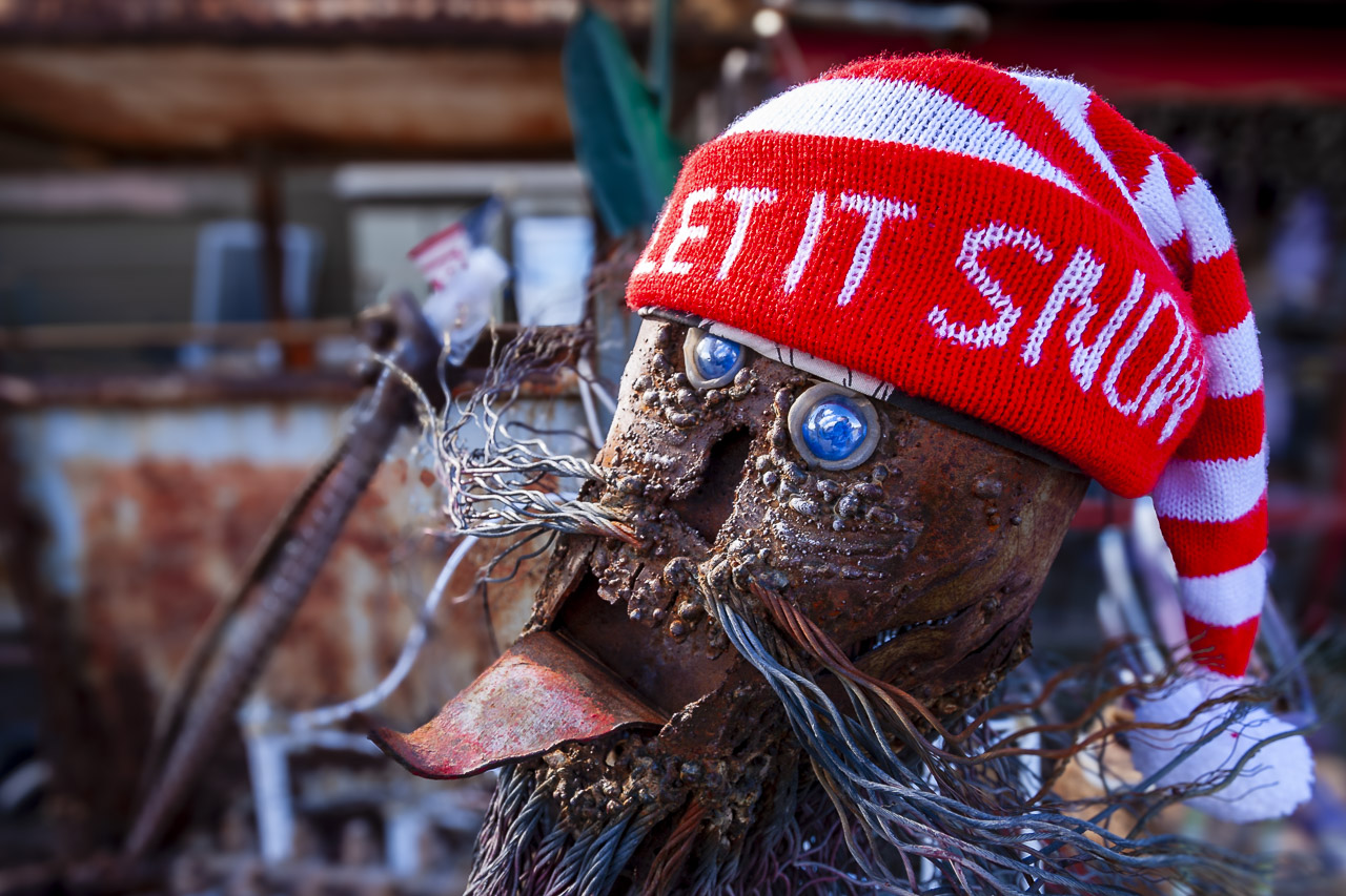 A metal head with whiskers and a mouth with his tongue sticking out and a hat saying, "Let it snow".