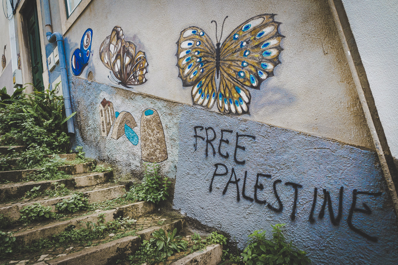 The steps at the bottom of the Escadinhas Damasceno Monteiro in Lisbon. Beautiful butterfly graffiti and a crudely written "FREE PALESTINE" on the wall.