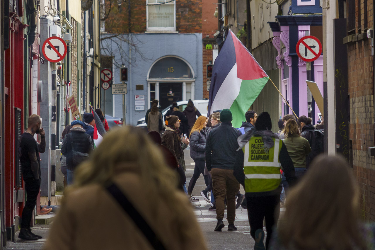 The view down Robert Street where the rally doubled back through Oliver Plunkett Street. People walking and some carrying flags and banners.