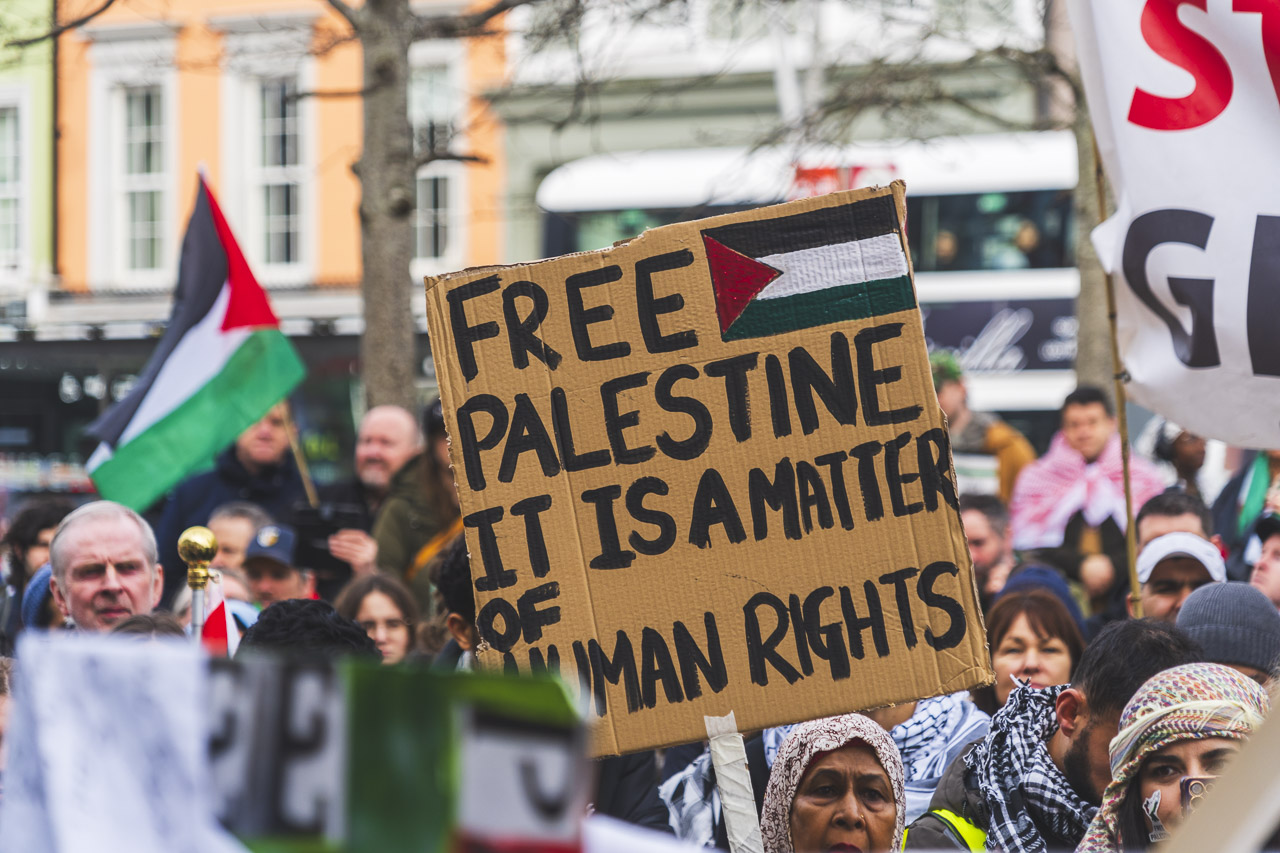 A woman at the rally holds up a sign saying, "FREE PALESTINE IT IS A MATTER OF HUMAN RIGHTS"