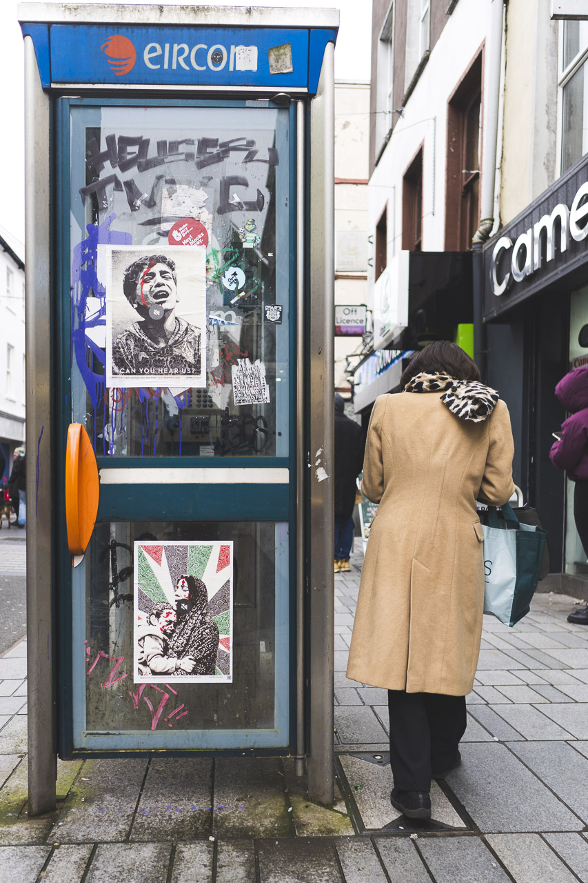 A woman walks past an Eircom phone box vandalised by graffiti and displaying pro-Gaza stickers.