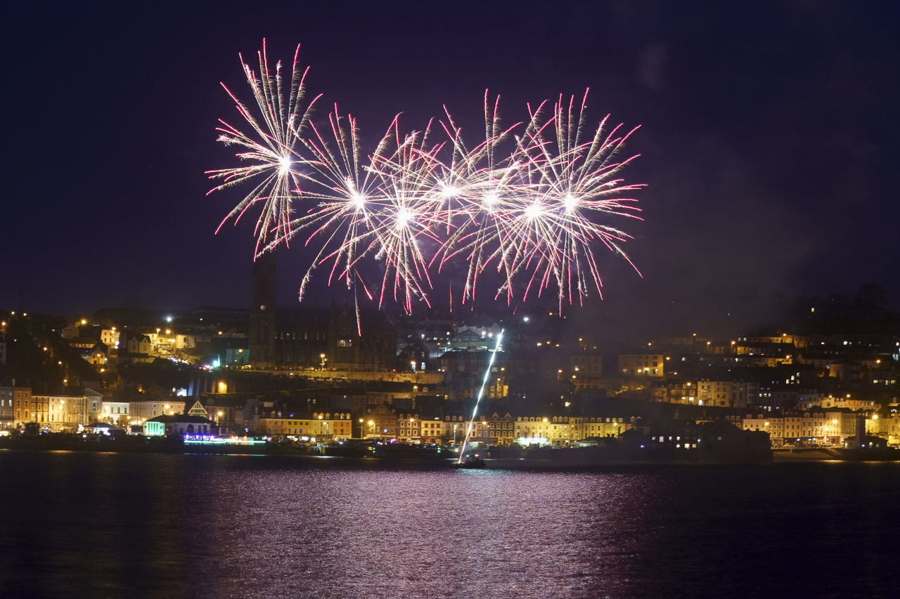 Fireworks light up the night sky over Cobh. The light reflects on the water.