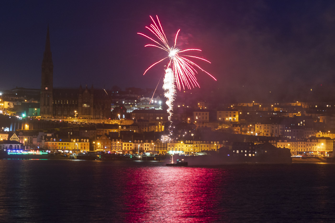 Fireworks light up the night sky over Cobh. The light reflects on the water.