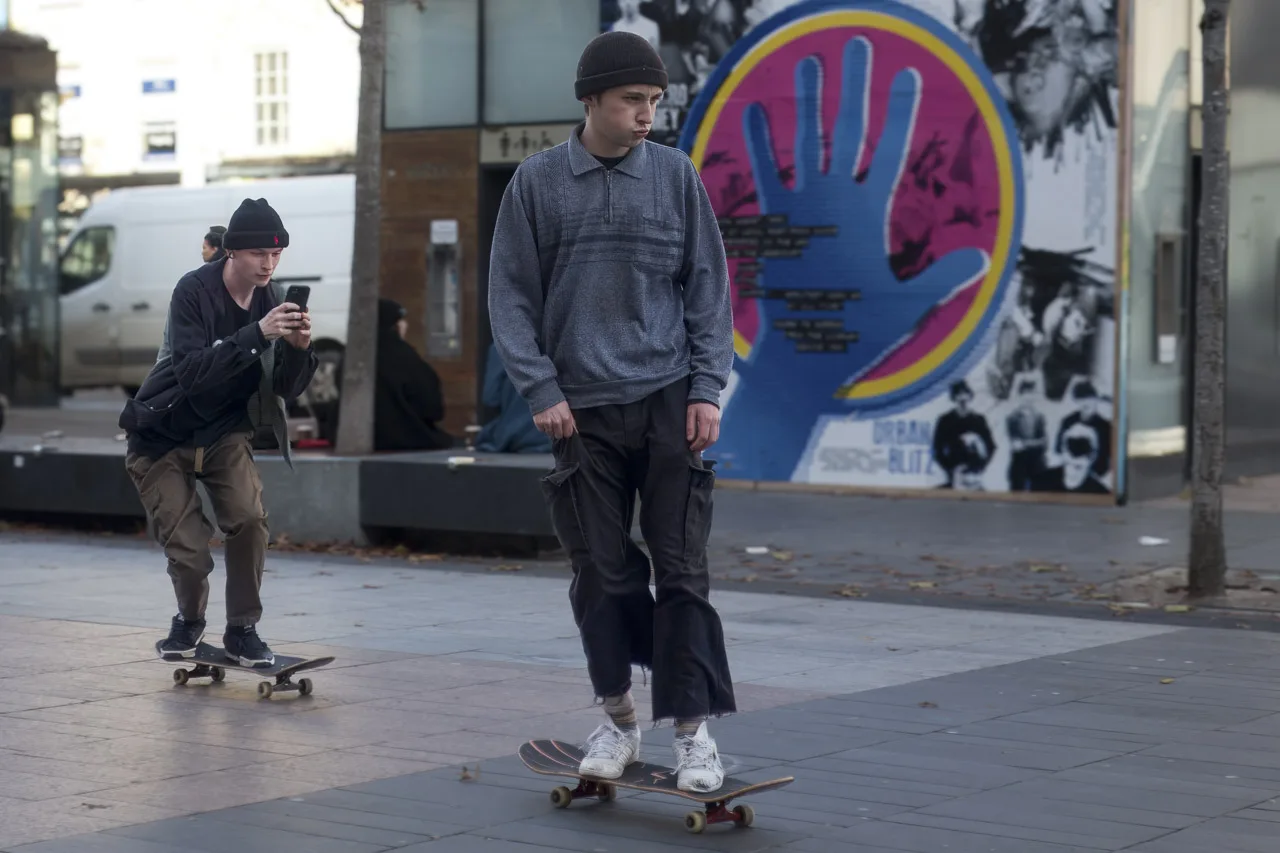 Two young men on skateboards, one filming the other with his phone.