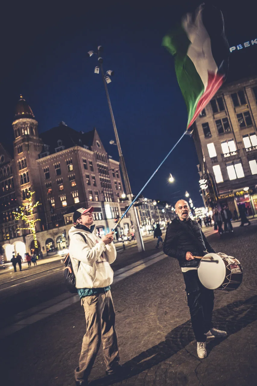 Two protestors, one beating a drum while the other waves the flag of Palestine.