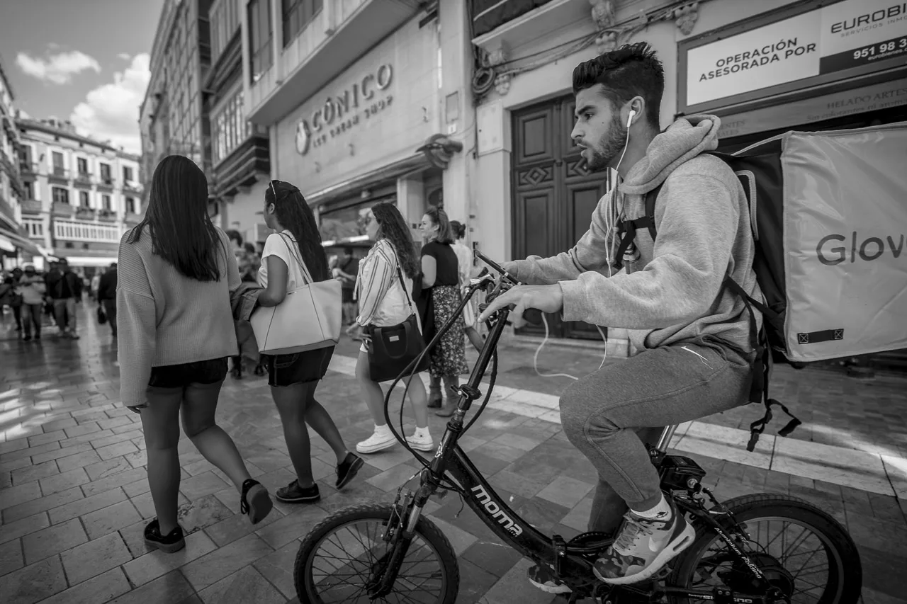 A young man on a bike weaves through the pedestrian traffic behind a group of women walking in front of him, and just in front of me, the photographer.