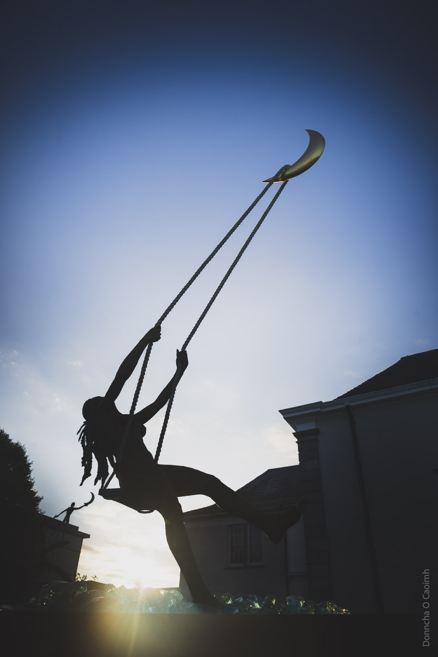 A statue of a woman playing on a swing suspended by rope on the Moon.