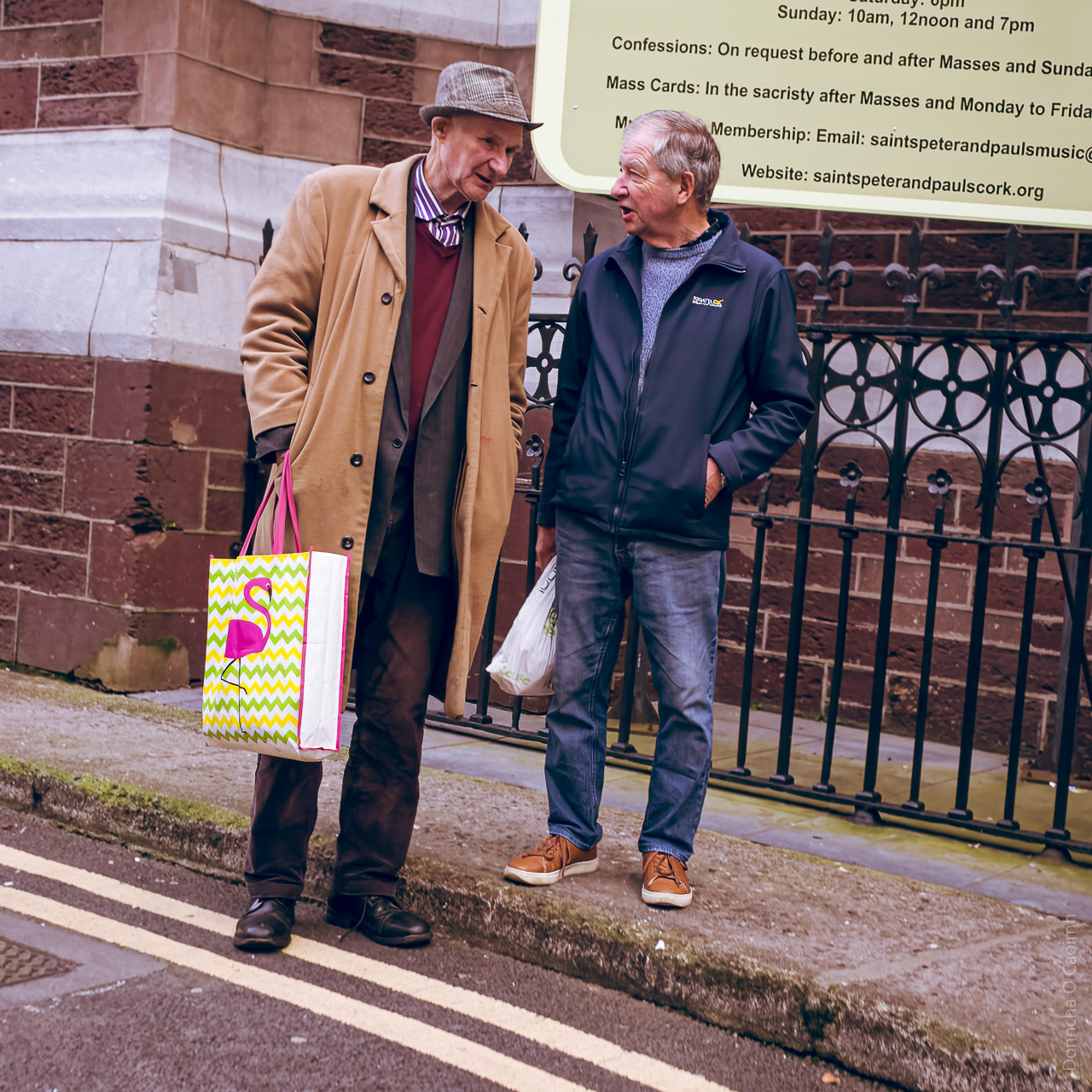 Two men talking on the street. One taller than the other is standing on the street, while the other stands on the pavement.