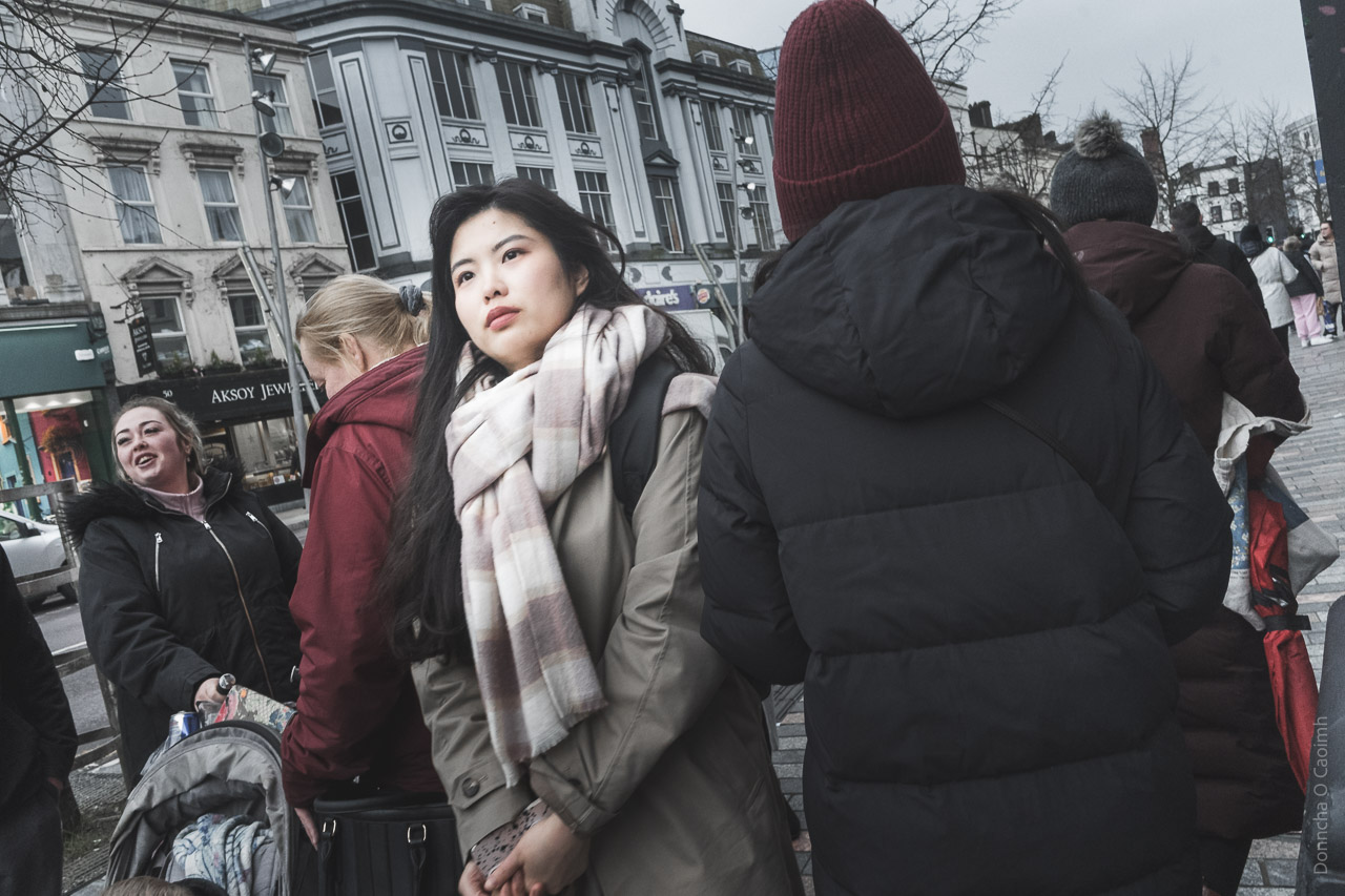 A woman walks between others on the street. Everyone has a coat on as it's a chilly March day.